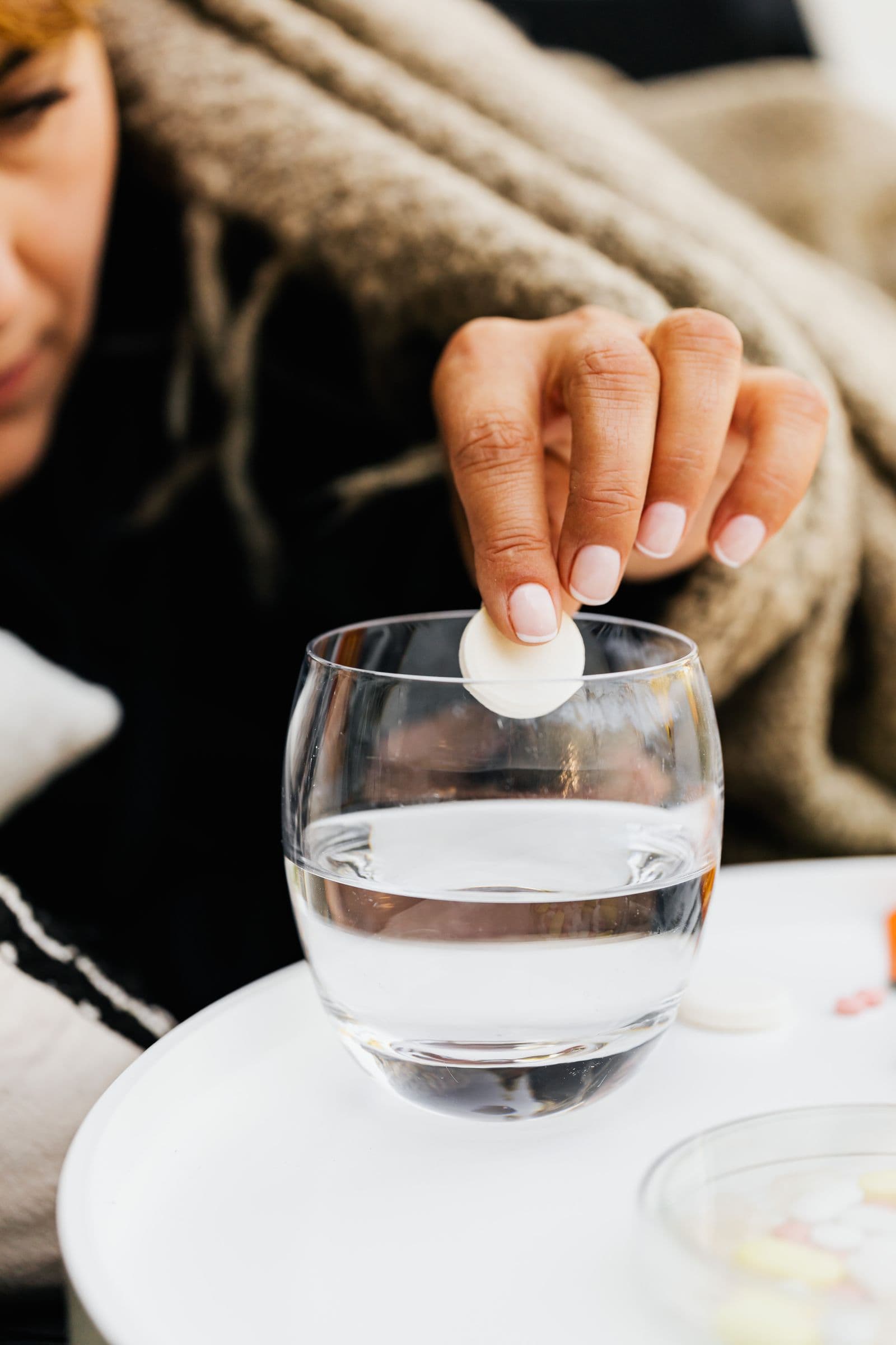 Main déposant une pastille effervescente d'électrolytes dans un verre d'eau