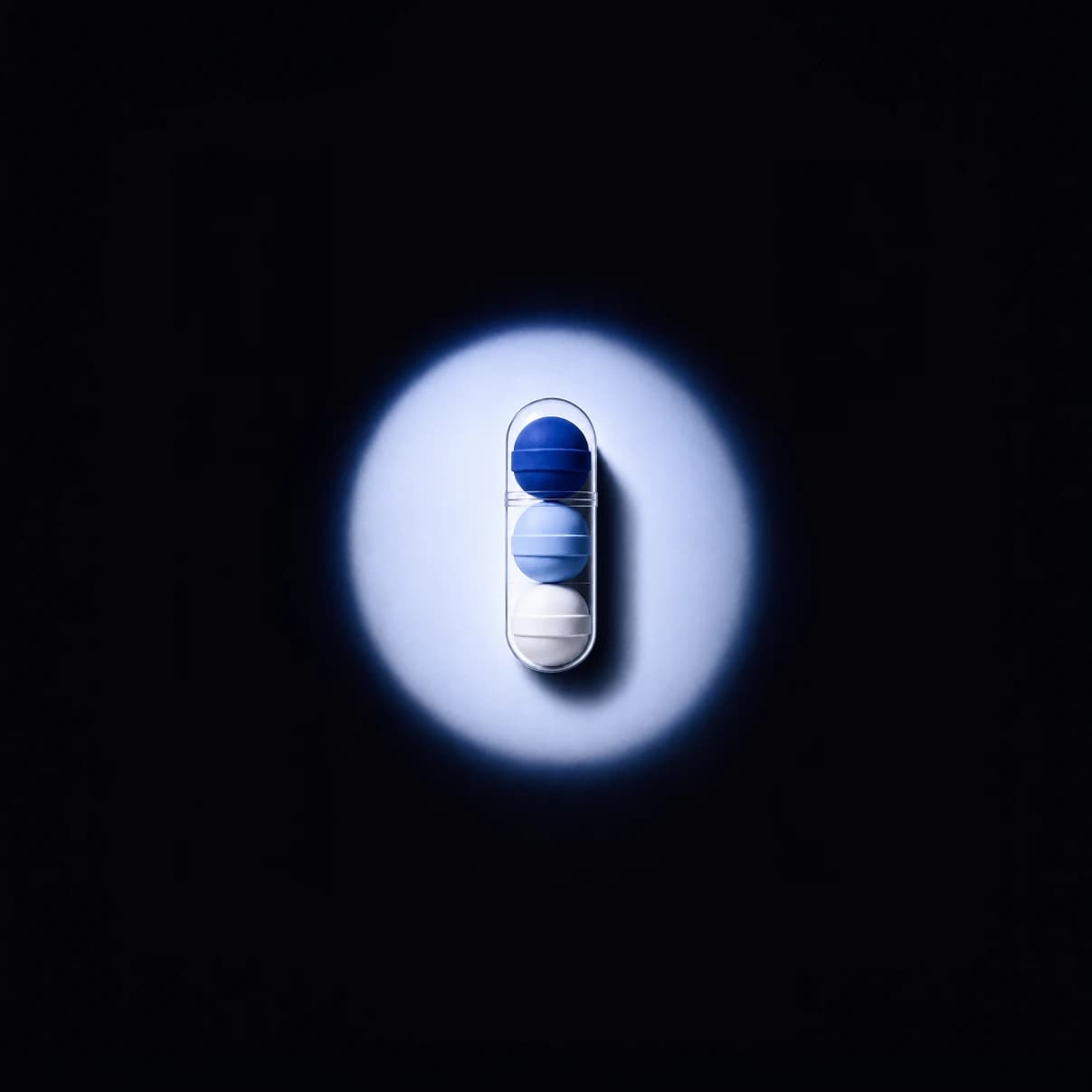 Une gélule SR-3C éclairée dans l'obscurité, ses 3 billes visibles